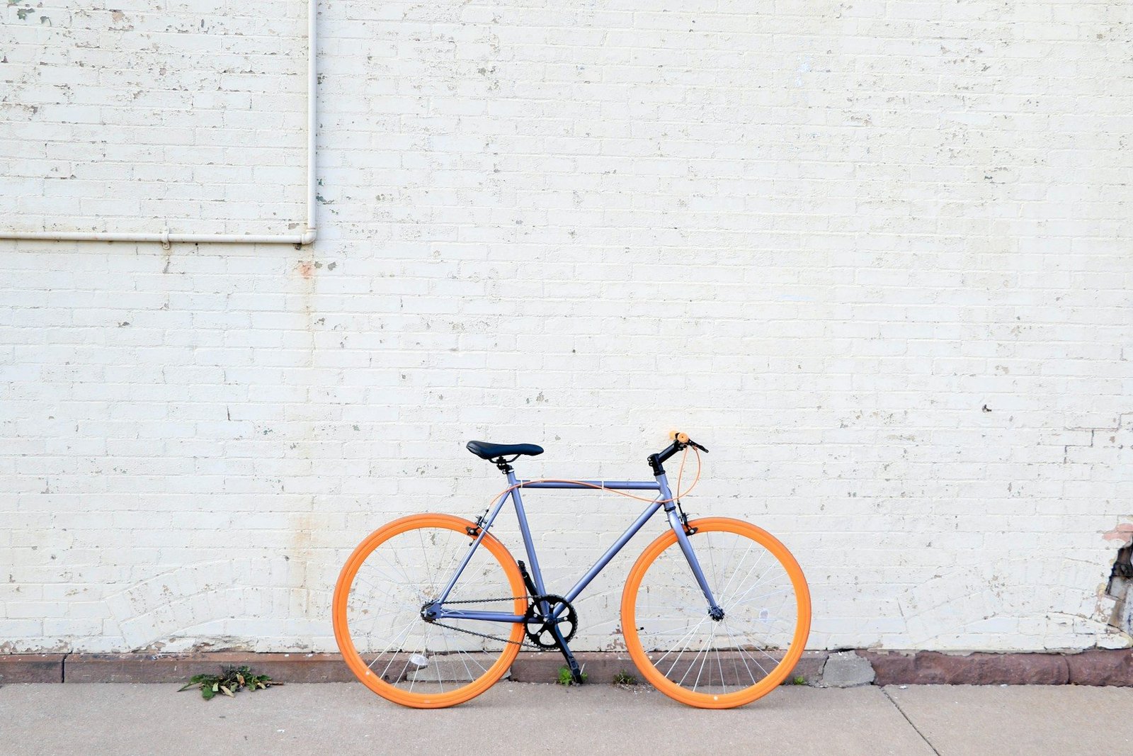 A grey city bicycle with bright orange tyres leaning against a white brick wall